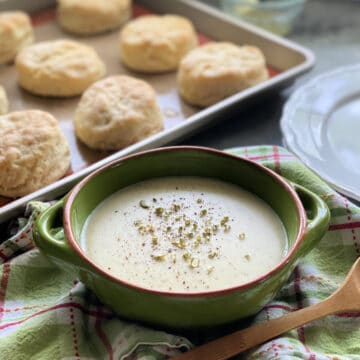 Green bowl filled with white gravy and a tray of biscuits next to the gravy bowl.