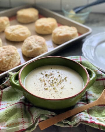 Green bowl filled with white gravy and a tray of biscuits next to the gravy bowl.