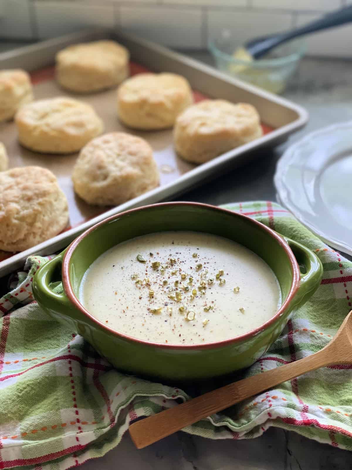 Green bowl filled with white gravy and a tray of biscuits next to the gravy bowl.