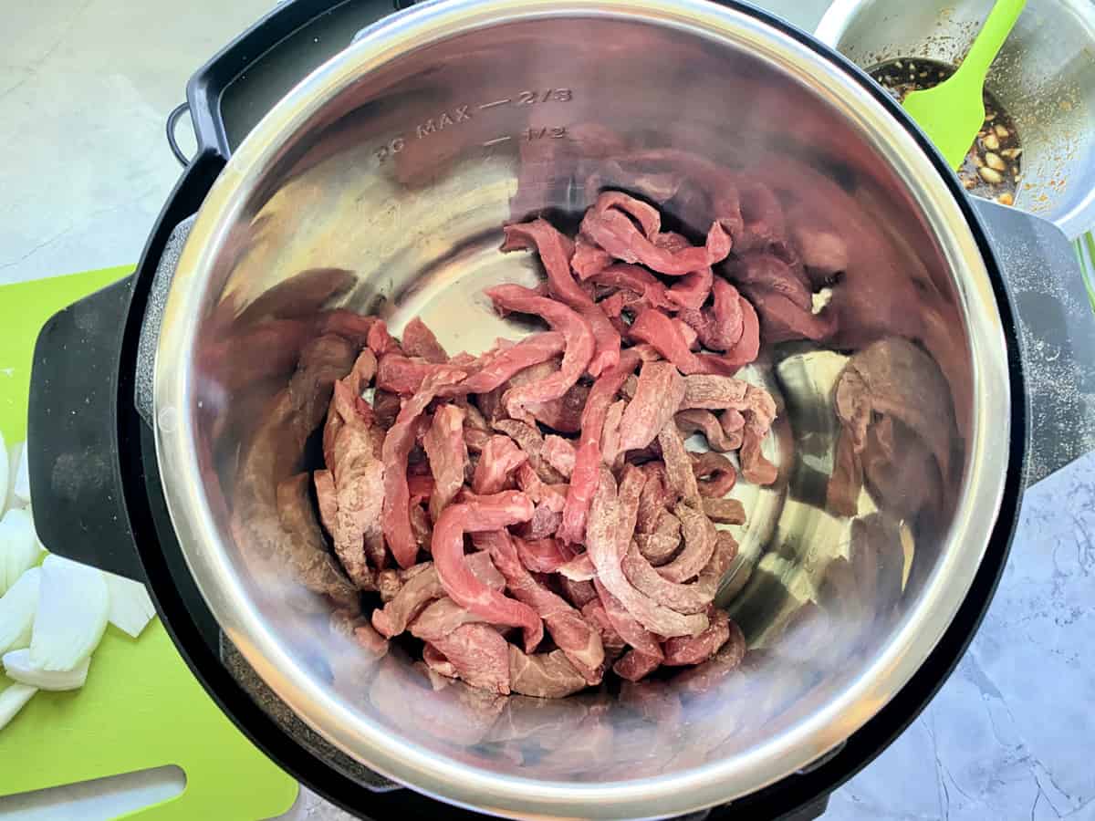 Top view of strips of raw beef in an Instant Pot.