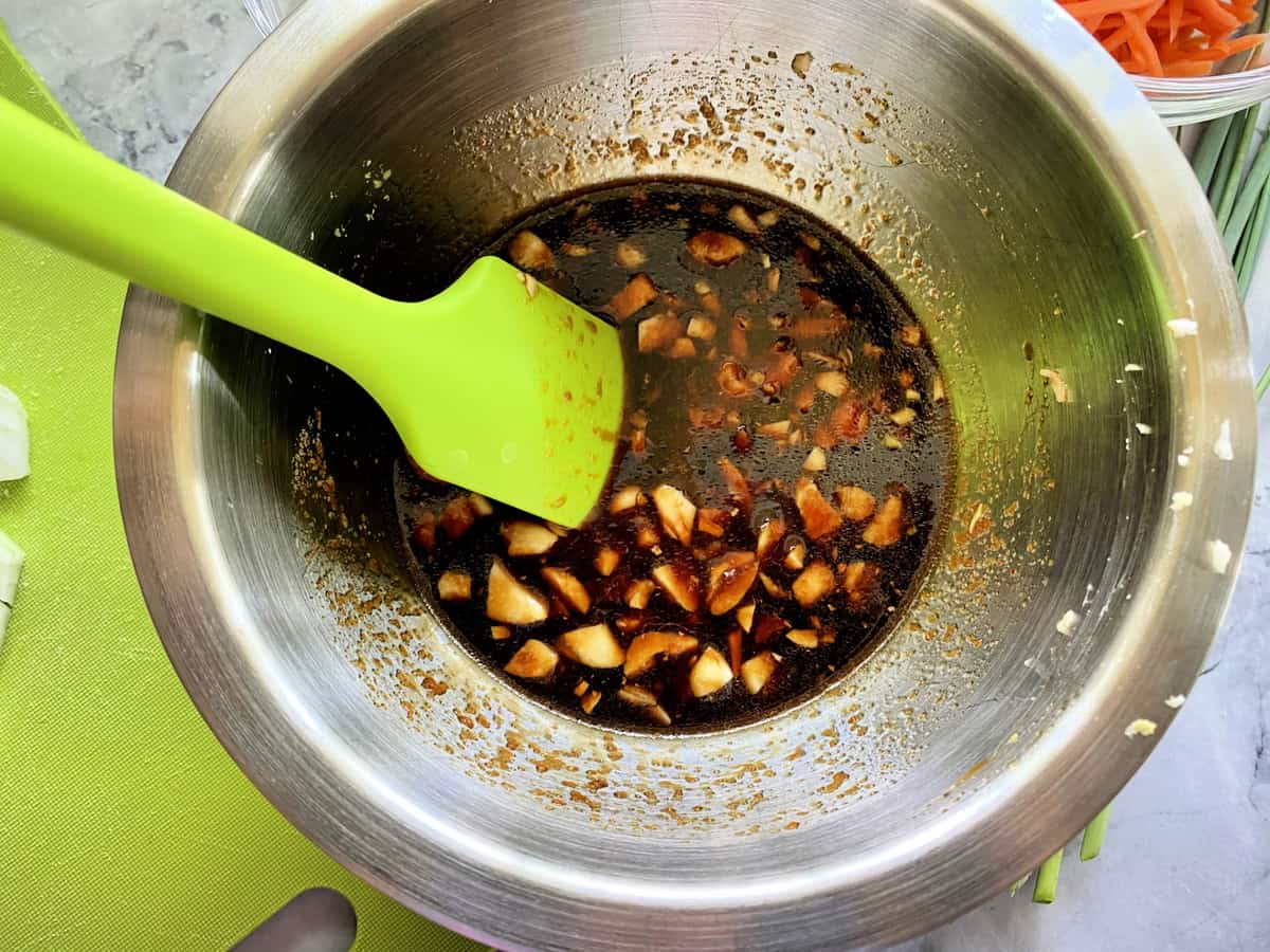 Top view of a stainless steel bowl with liquid and a silicone mixing spoon.