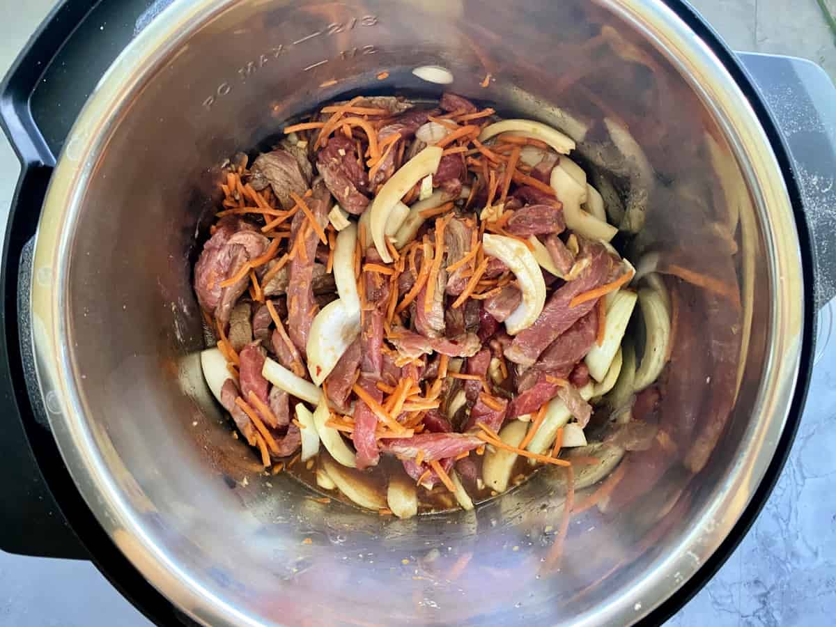 Top view of an Instant Pot with mixed beef, carrots, and onions in sauce.