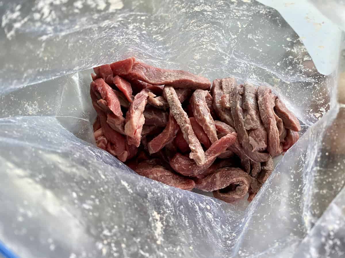 Top view of a plastic bag with strips of beef coated in cornstarch.