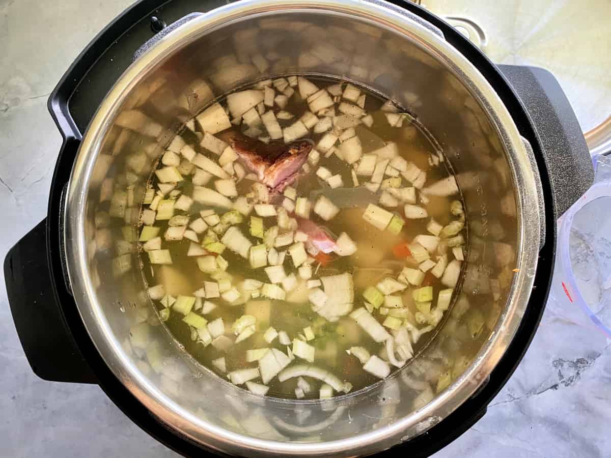 Top view of an Instant Pot with liquid and chopped veggies for soup.