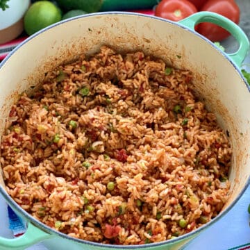 Green pot filled with Mexican Rice with vegetables on the side.
