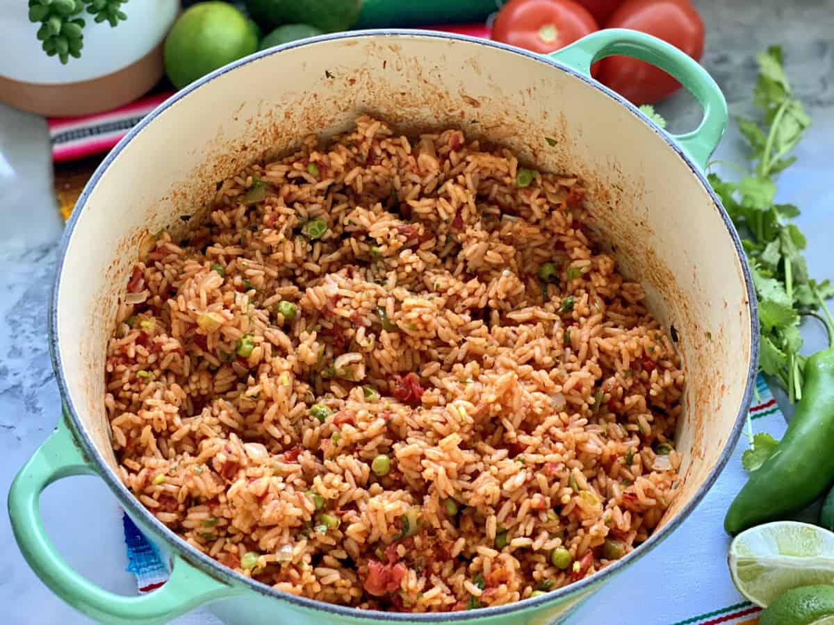 Green pot filled with Mexican Rice with vegetables on the side.