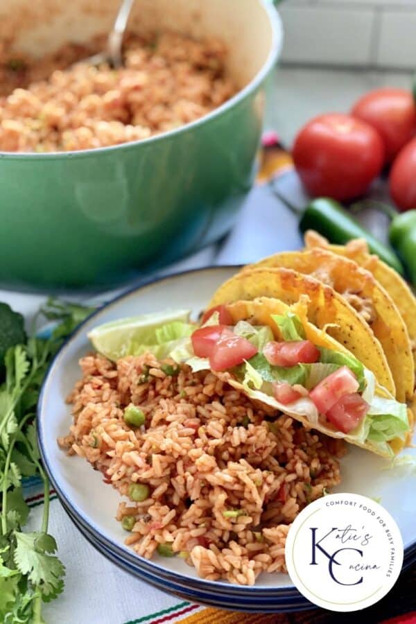 White plate filled with rice, tacos, and veggies and a pot in the background.