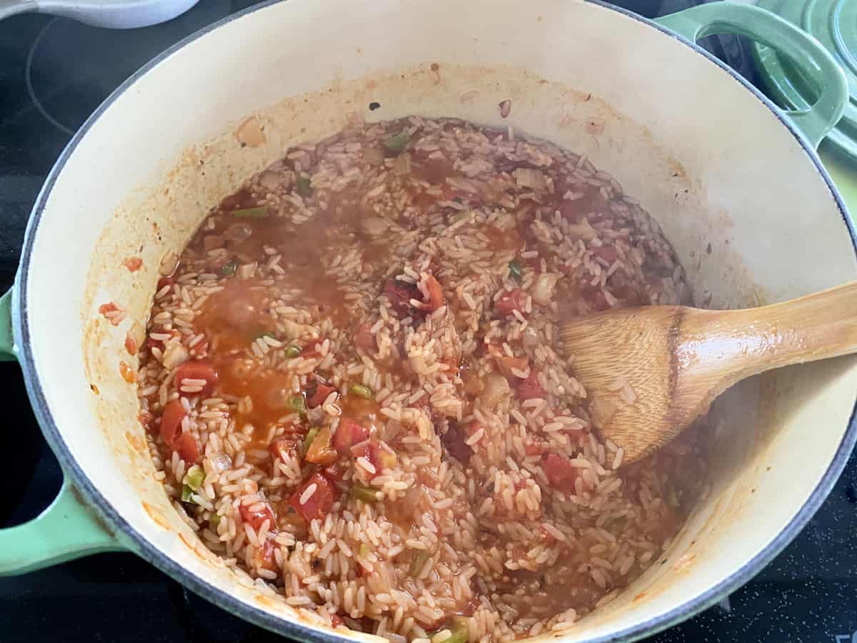 Sauce pot with rice and tomatoes with wooden spoon in pot.