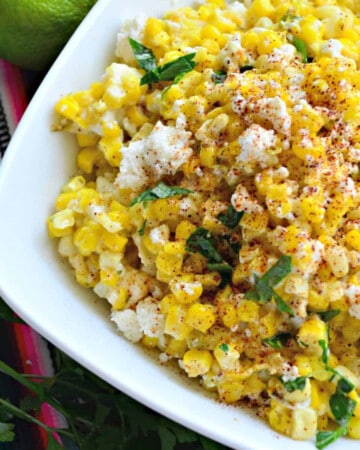 White square bowl filled with corn, cheese, and herbs.