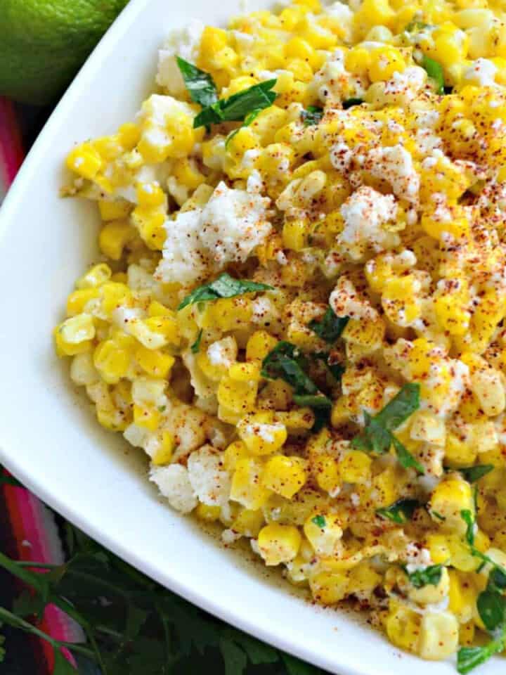 White square bowl filled with corn, cheese, and herbs.