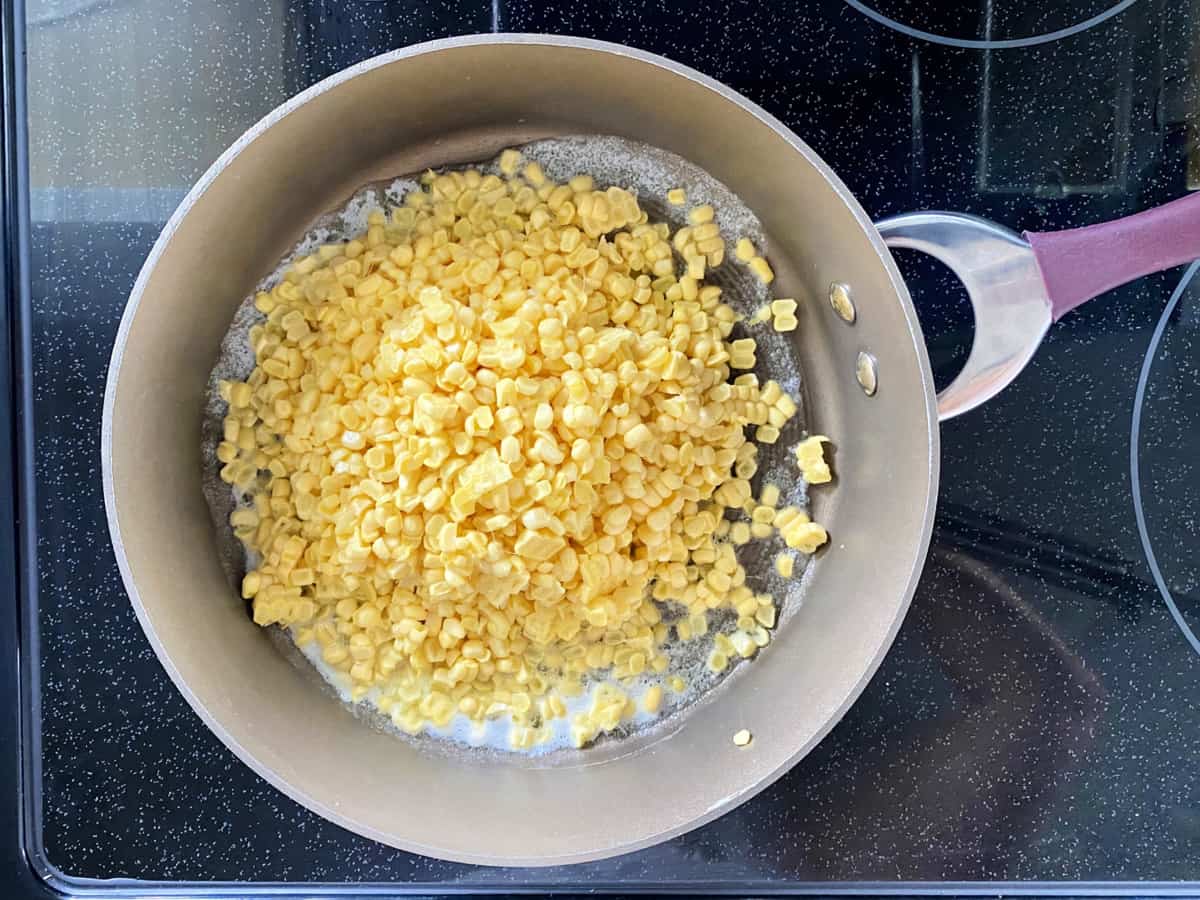 Top view of a skillet with melted butter and fresh corn kernels.