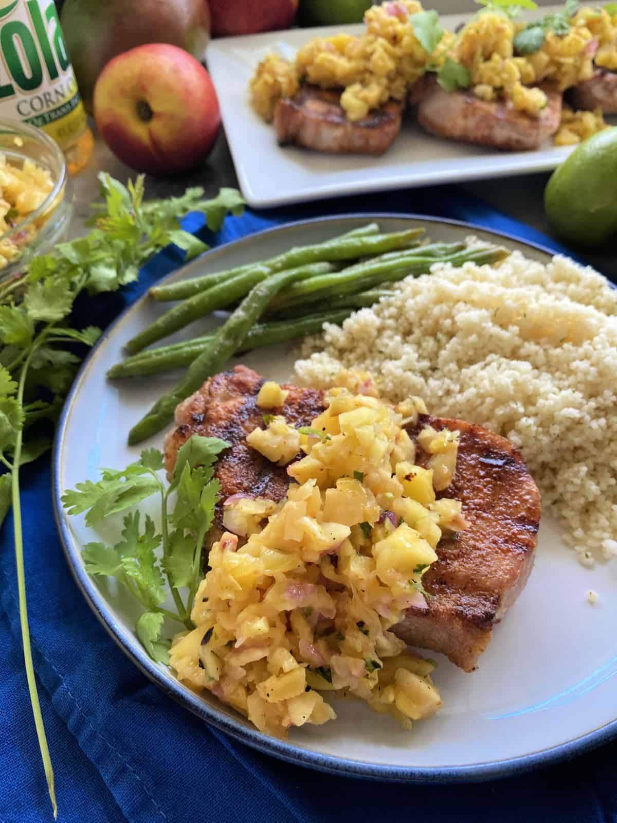 Plate of pork chop with fruit salsa, cilantro, couscous, and green beans.