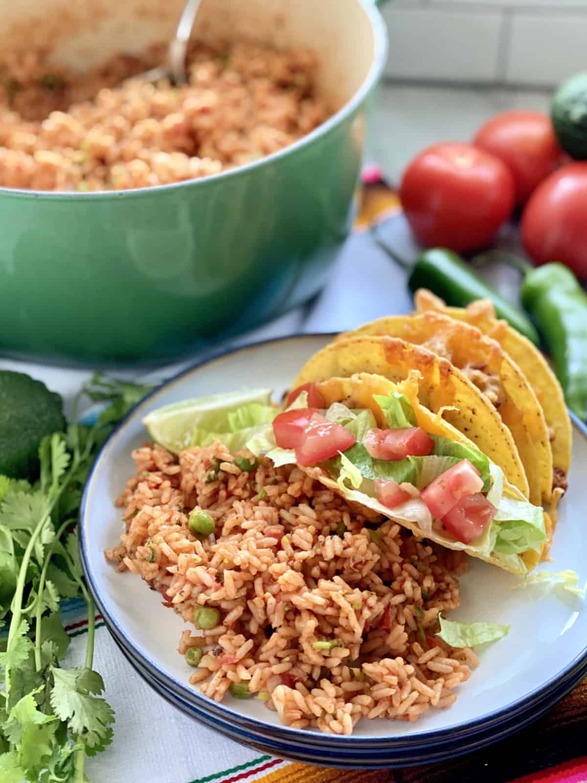 White plate filled with Mexican Rice and tacos with greep pot filled with rice in background.