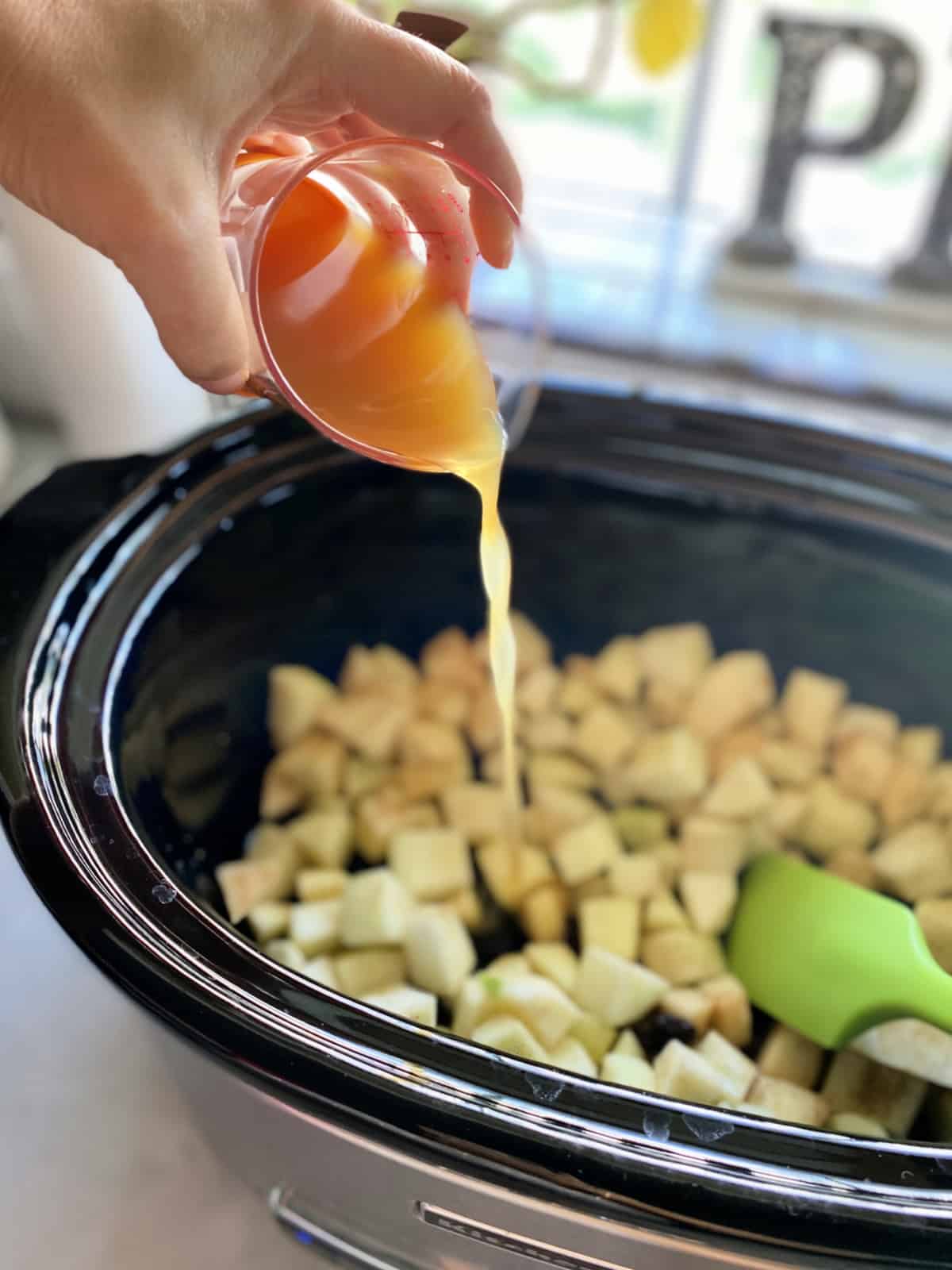 Female hand pouring apple juice into a crock pot filled with diced apples.