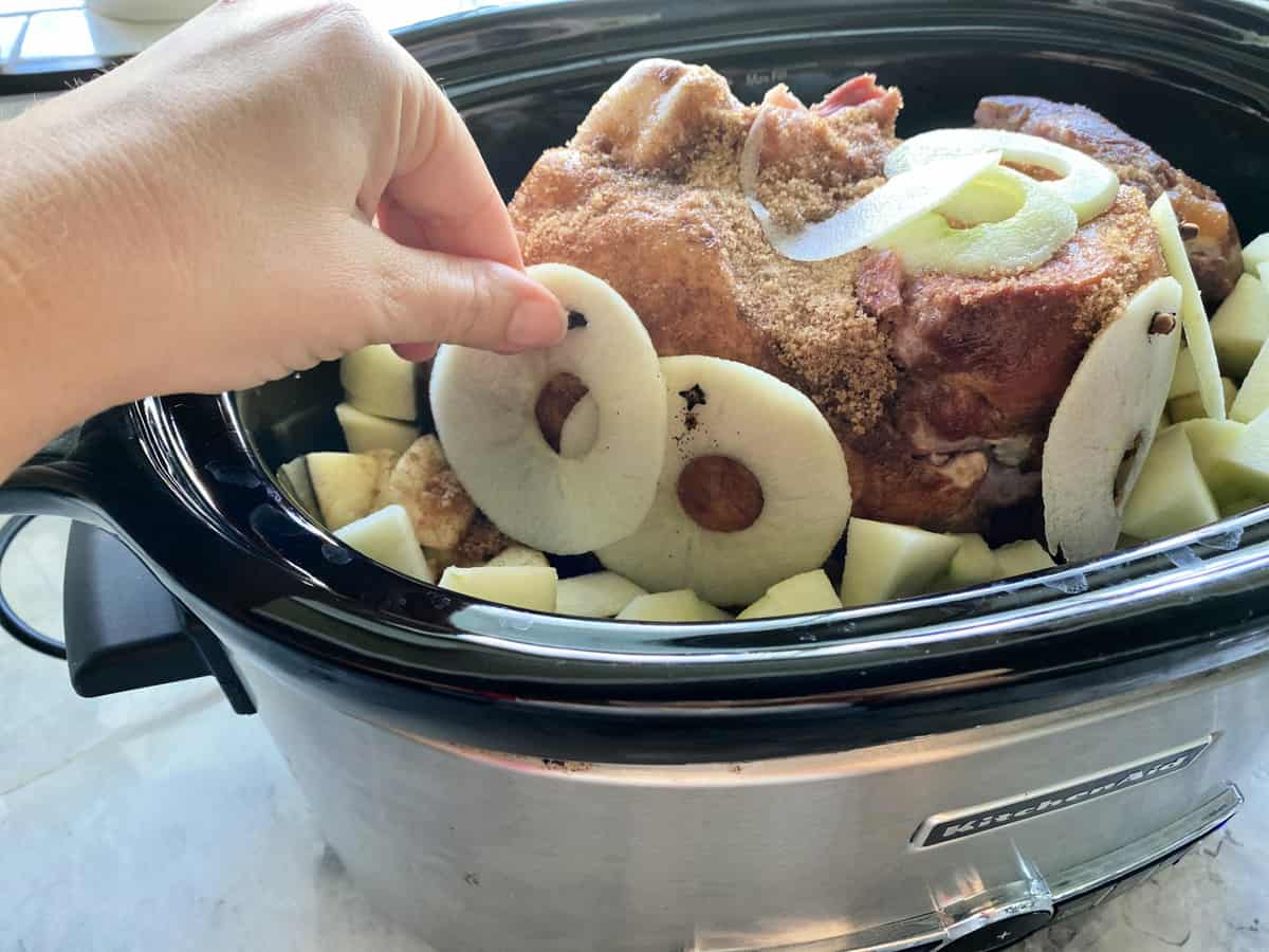 Female hand placing rings of apples onto a brown sugar rubbed ham.