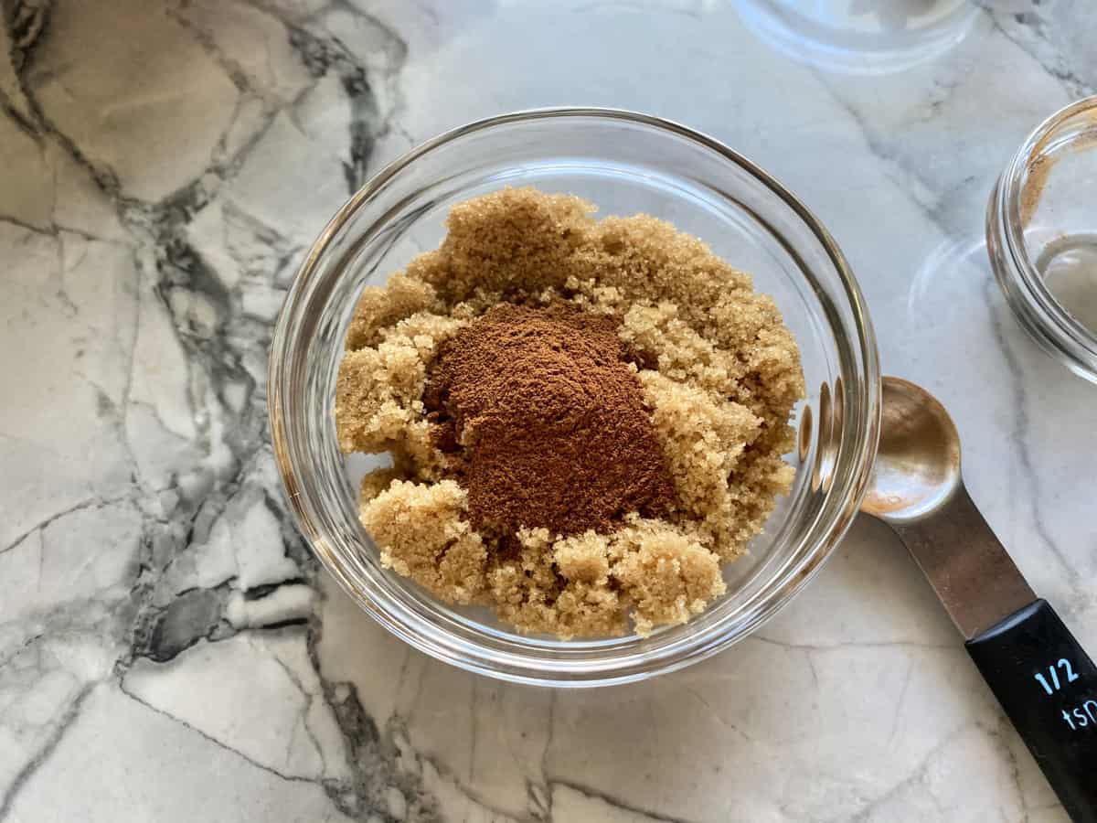 Top view of a glass bowl filled with brown sugar and cinnamon with a ½ teaspoon next to the bowl.