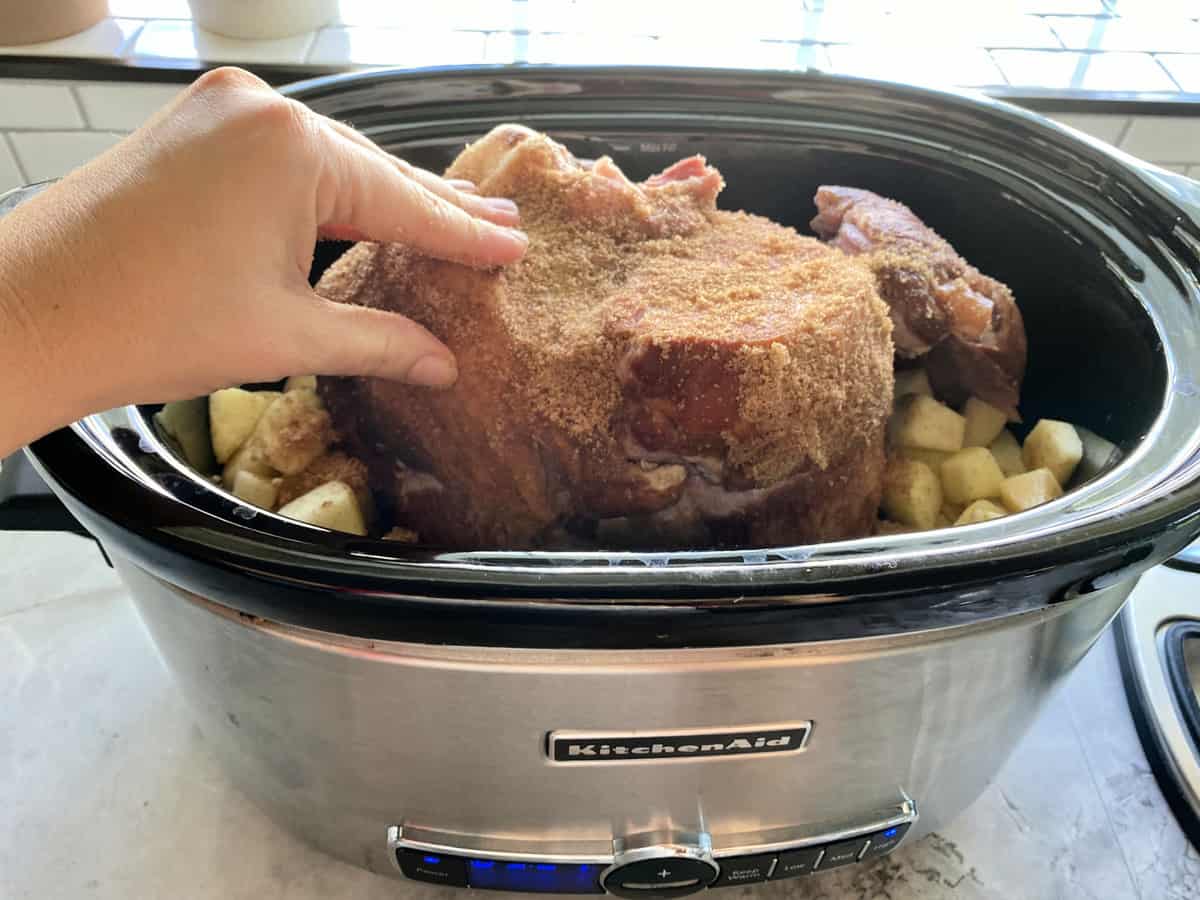 Female hand massaging brown sugar rub on to a ham in the slow cooker.
