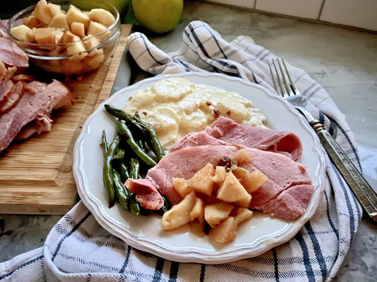 White plate filled with sliced ham, apples, green beans, and potatoes.