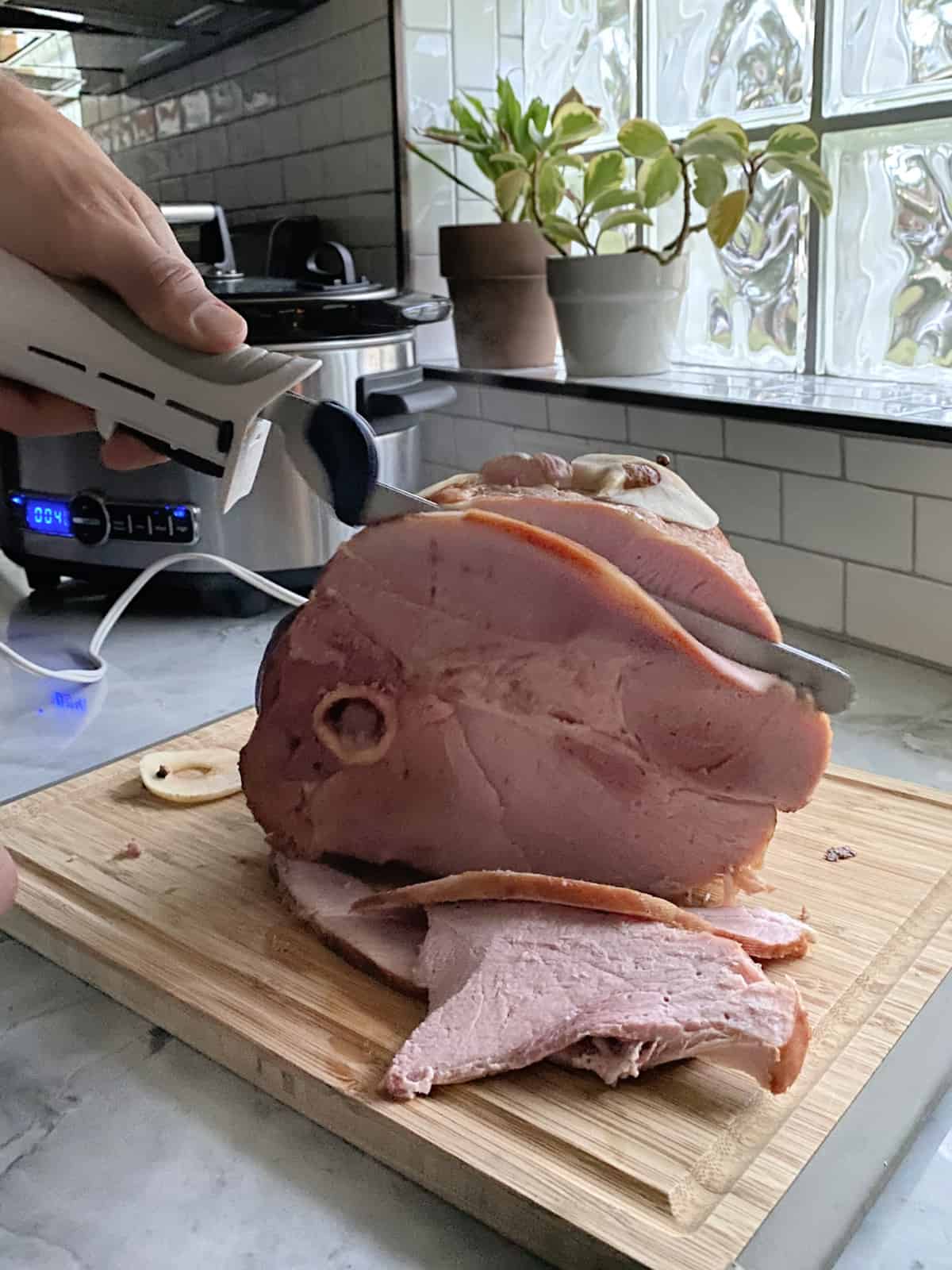 Male hand using an electric knife carving a half ham.