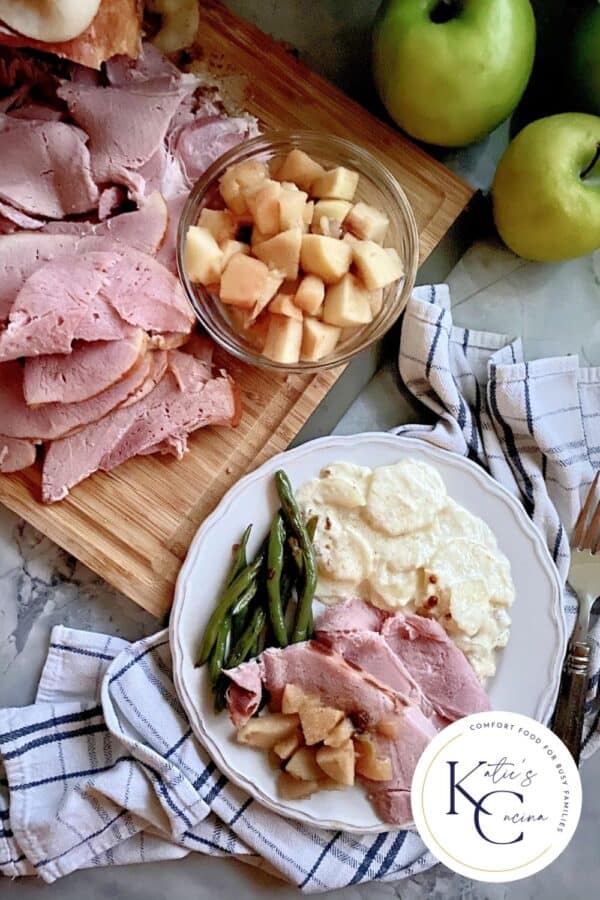 Top view of a ham dinner with potatoes, and green beans and sliced ham and apples on the side.