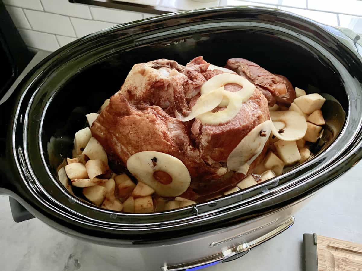 Slow cooker filled with a cooked half ham with apples.