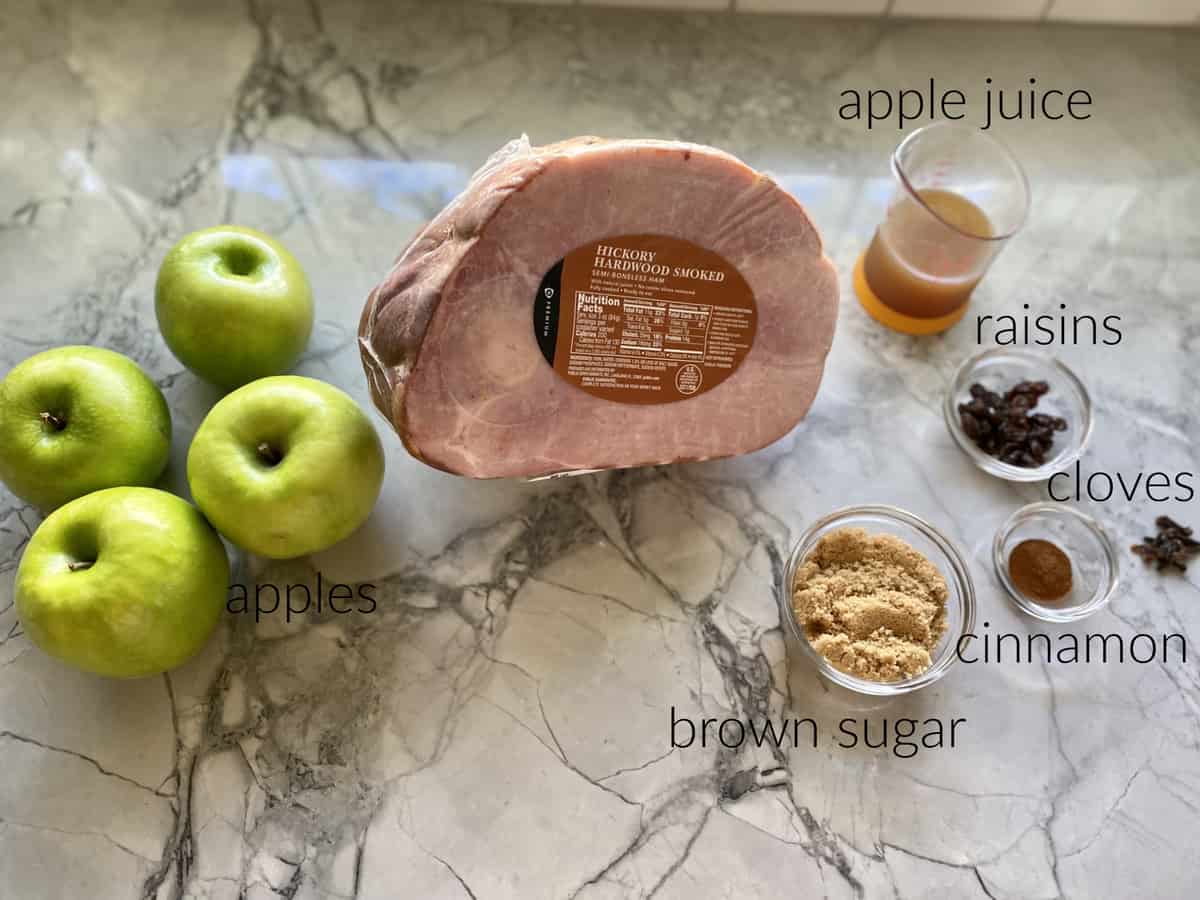 Ingredients on counterl ham, apple juice, apples, brown sugar, cinnamon, cloves, and raisins.