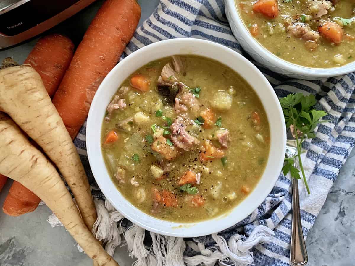 Top view of a white bowl of split pea soup with ham and vegetables with fresh vegetables next to it.