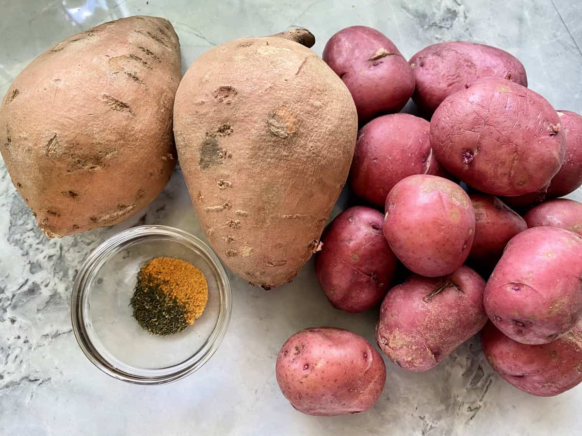 Ingredients on counter: two sweet potatoes, a dozen red potatoes and seasonings.