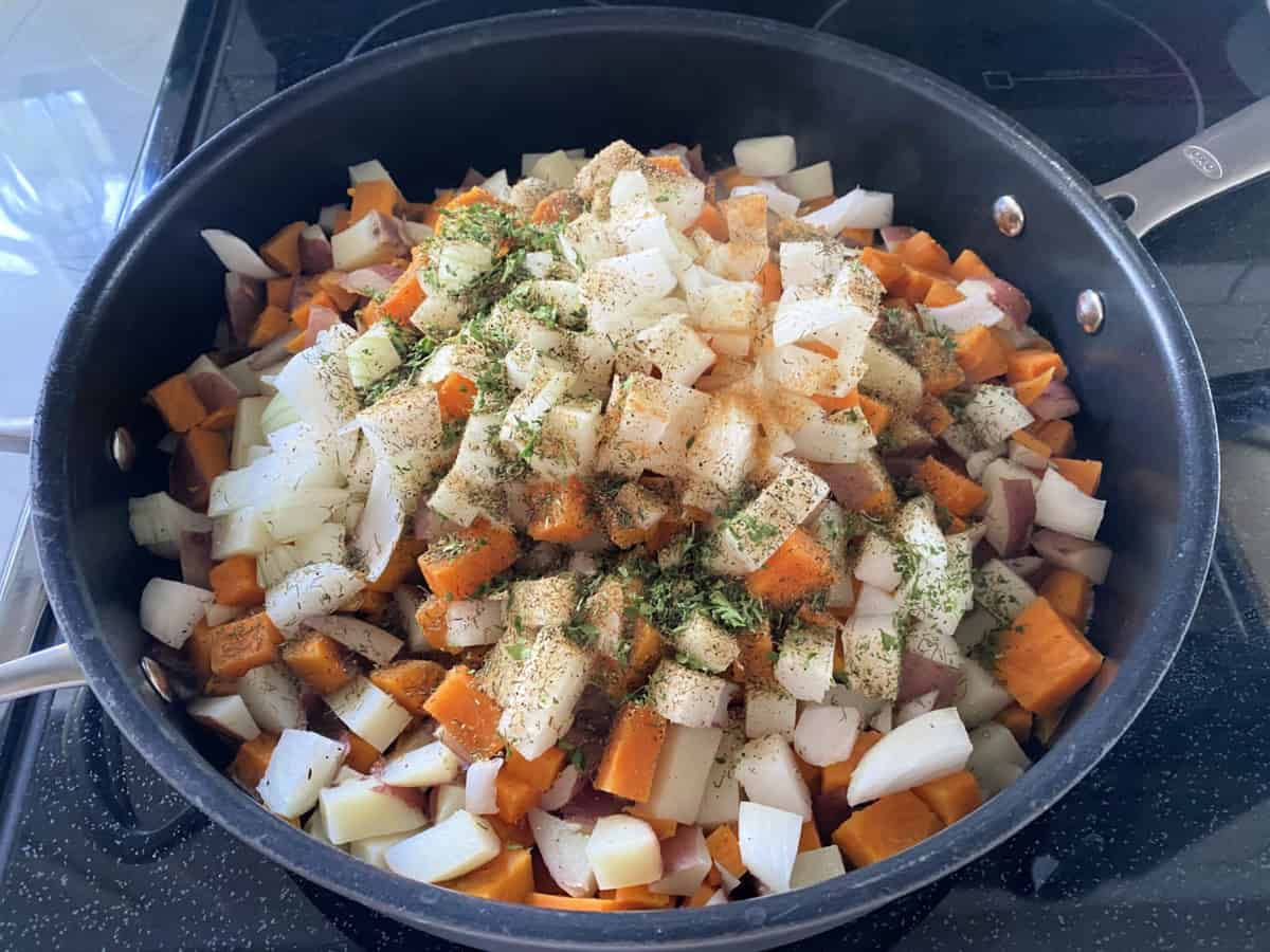 white and orange potatoes with seasoning and onions in a frying pan.