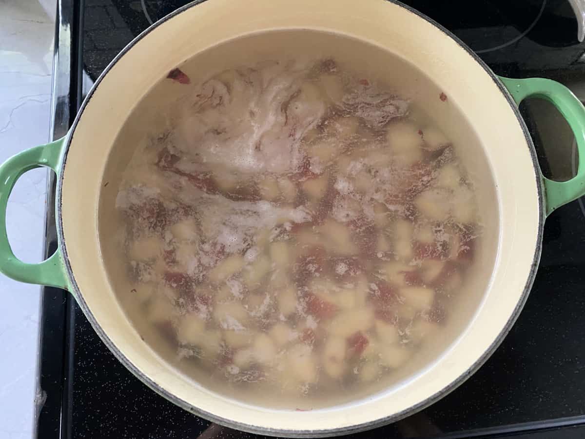 Top view of a green pot filled with water and potatoes boiling.