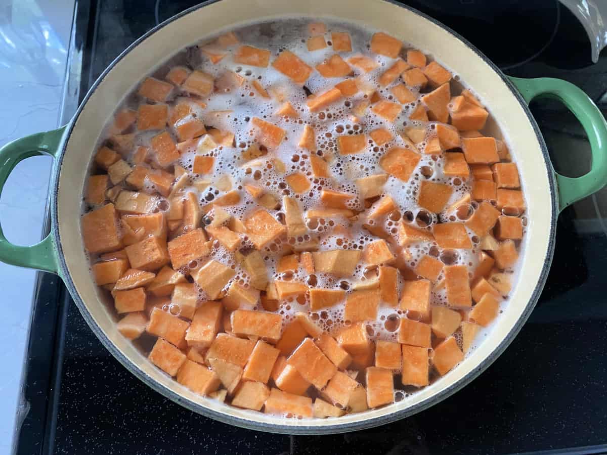 Top view of a green pot filled with diced sweet potatoes in water.