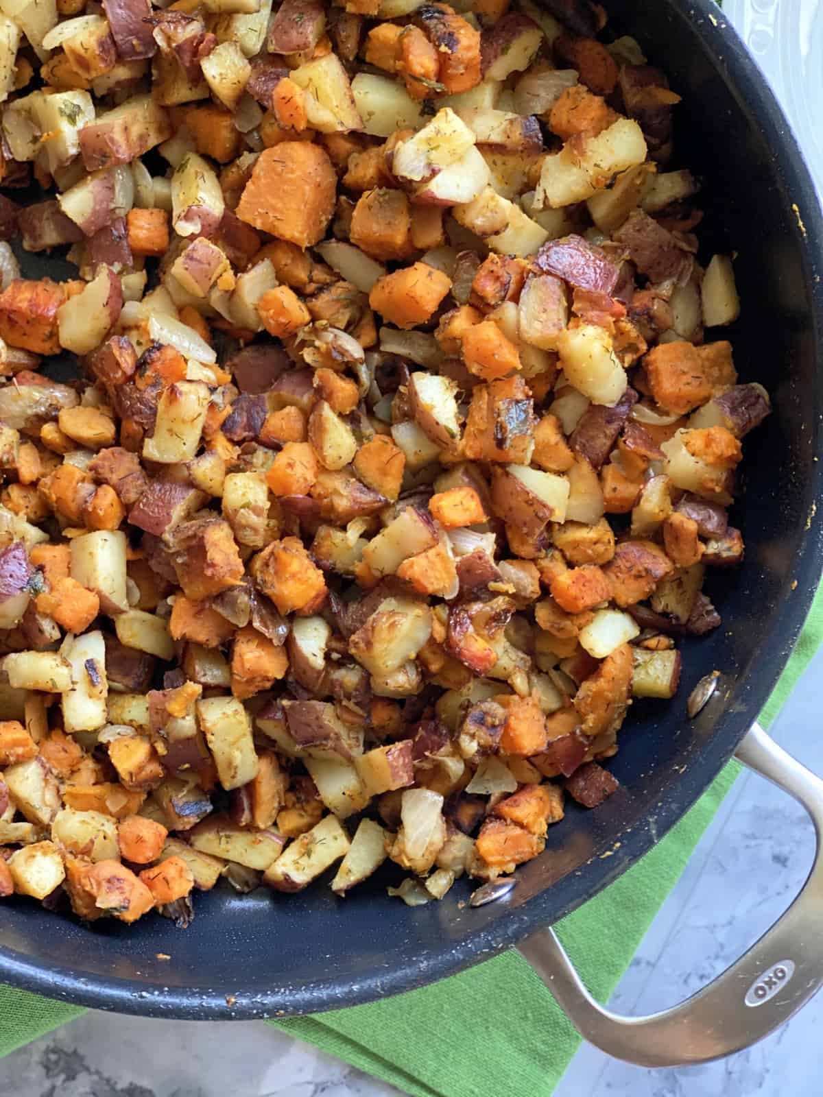 Top view of a skillet filled with fried sweet potatoes and white potatoes.