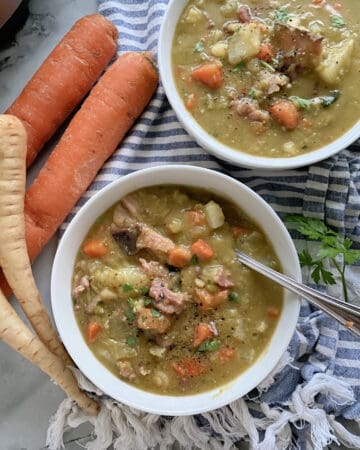 Top view of two white bowls filled with Split Pea Soup with ham and vegetables.