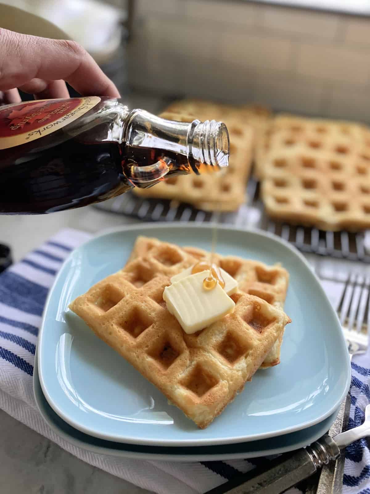 Male hand pouring maple syrip on to two waffles on a blue plate.