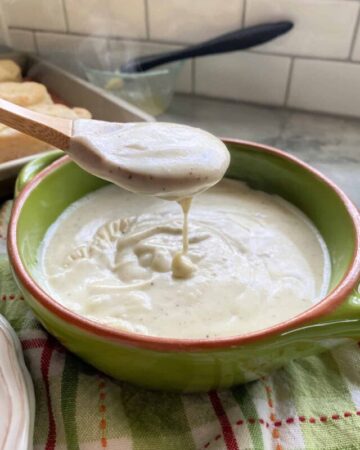 Wooden spoon drizzling white gravy into a green bowl full of white gravy.
