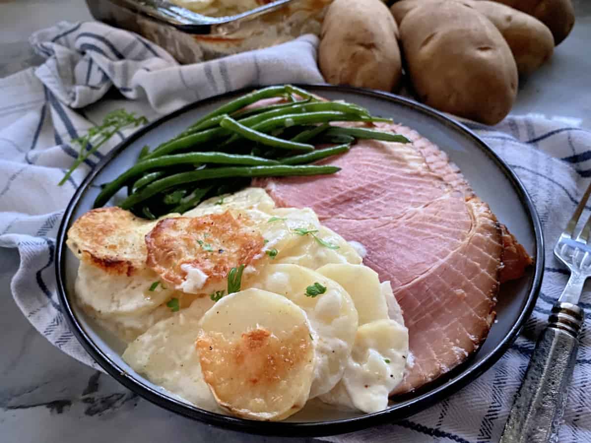 Plate filled with Gratin Dauphinois potatoes, green beans, and ham.