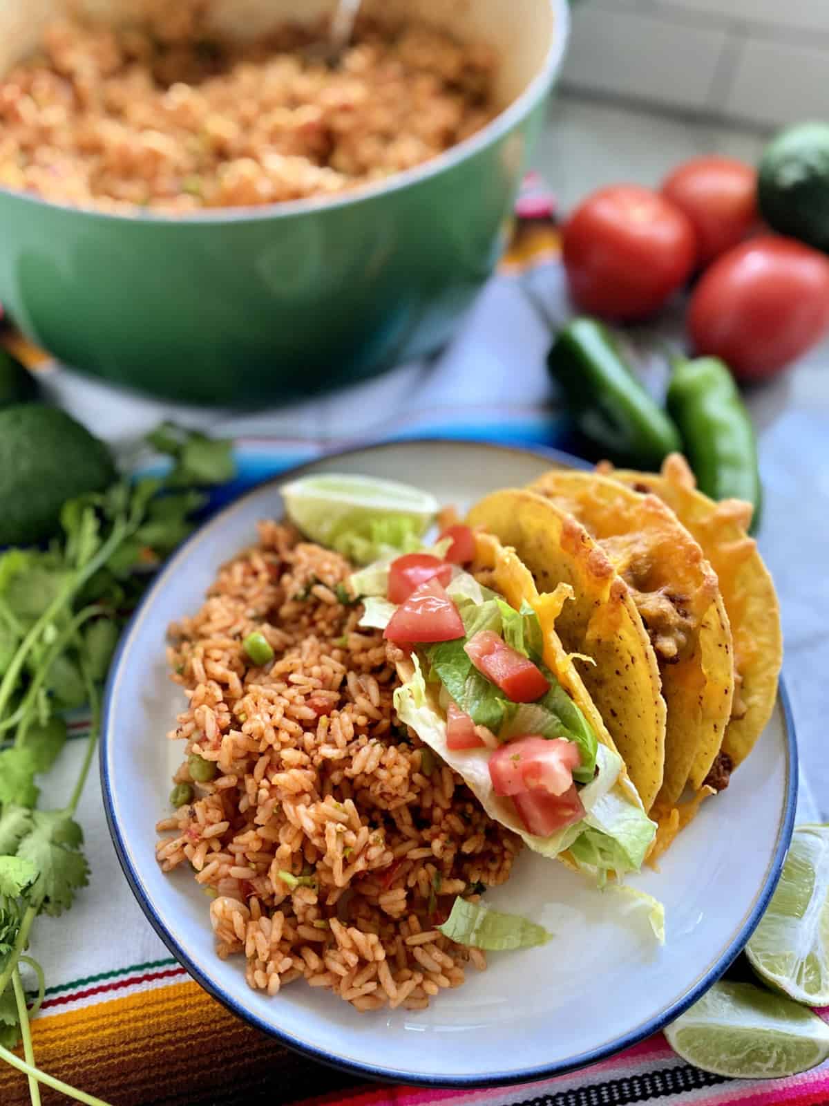 White plate filled with three tacos, Mexican Rice and vegetables in the background.