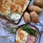 Top view of a baking dish filled with creamy potatoes, and a plate of dinner next to it.