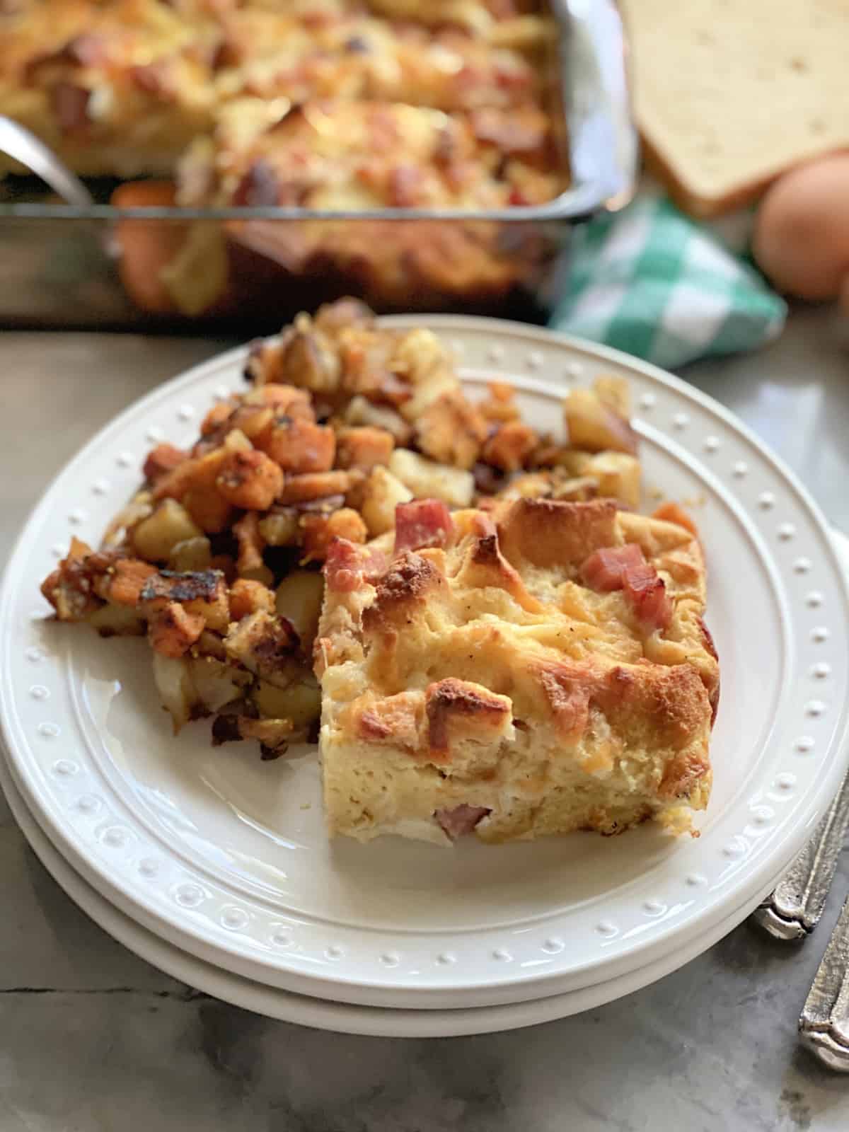 Two white plates stacked with a breakfast casserole slice and potatoes next to it.