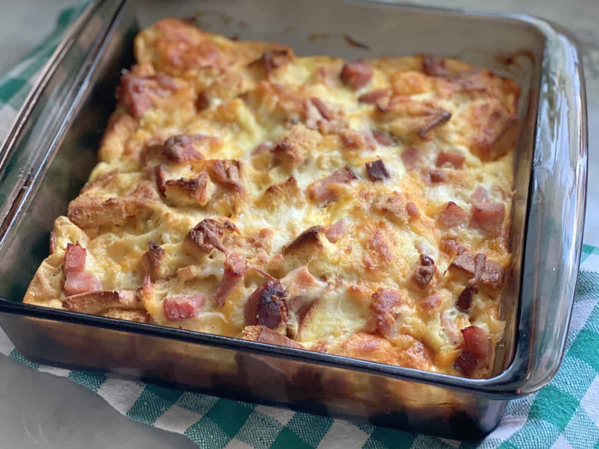 Square baking dish filled with eggs, ham, bread, and cheese.