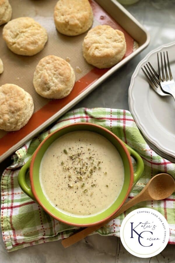 Top view of a green bowl filled with white gravy with a logo on the bottom right corner.