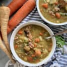 Top view of two white bowls filled with Split Pea Soup with ham and vegetables with a spoon in one bowl.