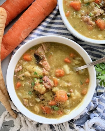 two white bowls filled with split pea soup with carrots and parsnips on the side.