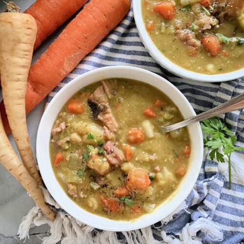 two white bowls filled with split pea soup with carrots and parsnips on the side.