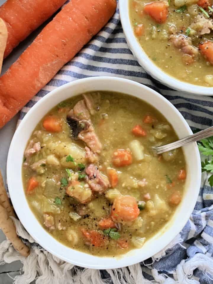 two white bowls filled with split pea soup with carrots and parsnips on the side.