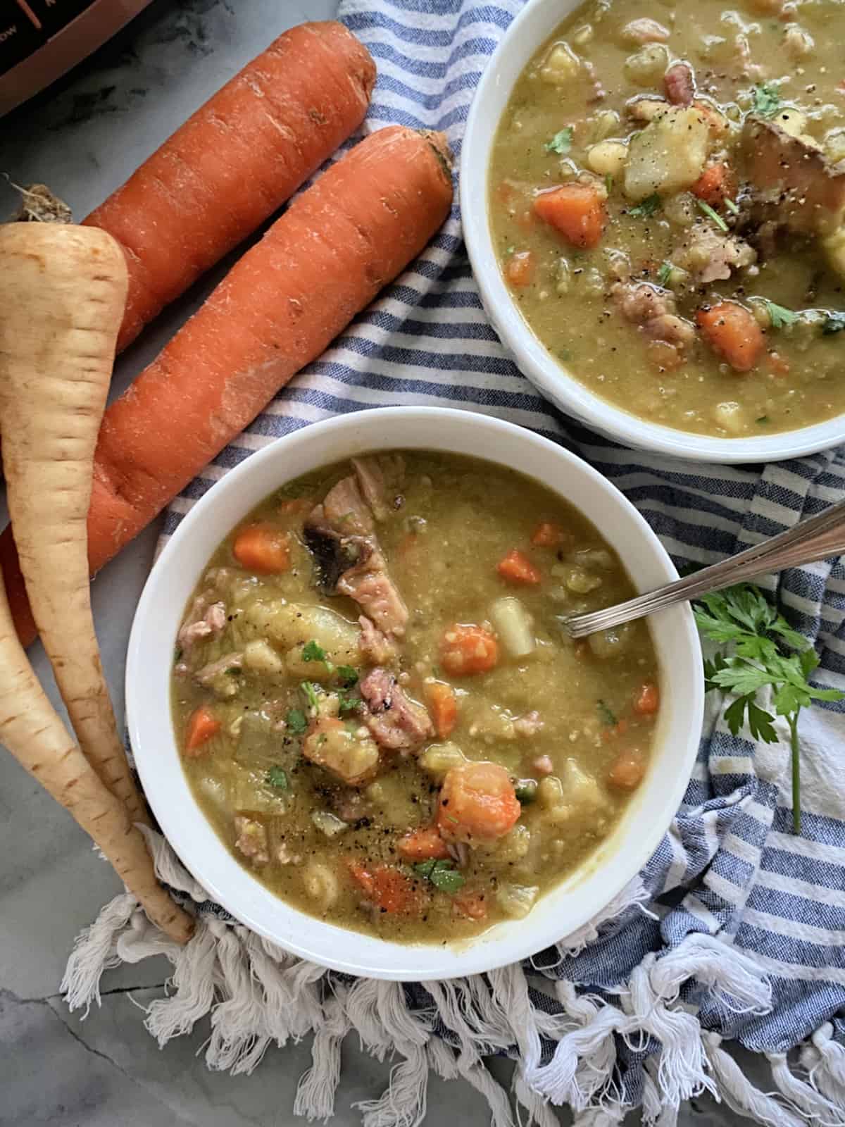 Top view of two white bowls filled with Split Pea Soup with ham and vegetables with a spoon in one bowl.