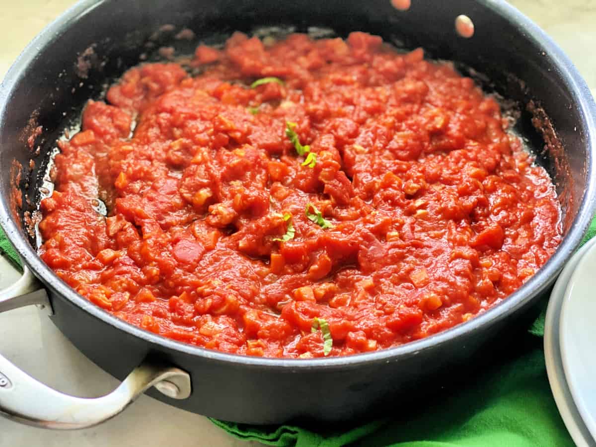 Black pot on a green cloth filled with thick red sauce and basil threads.