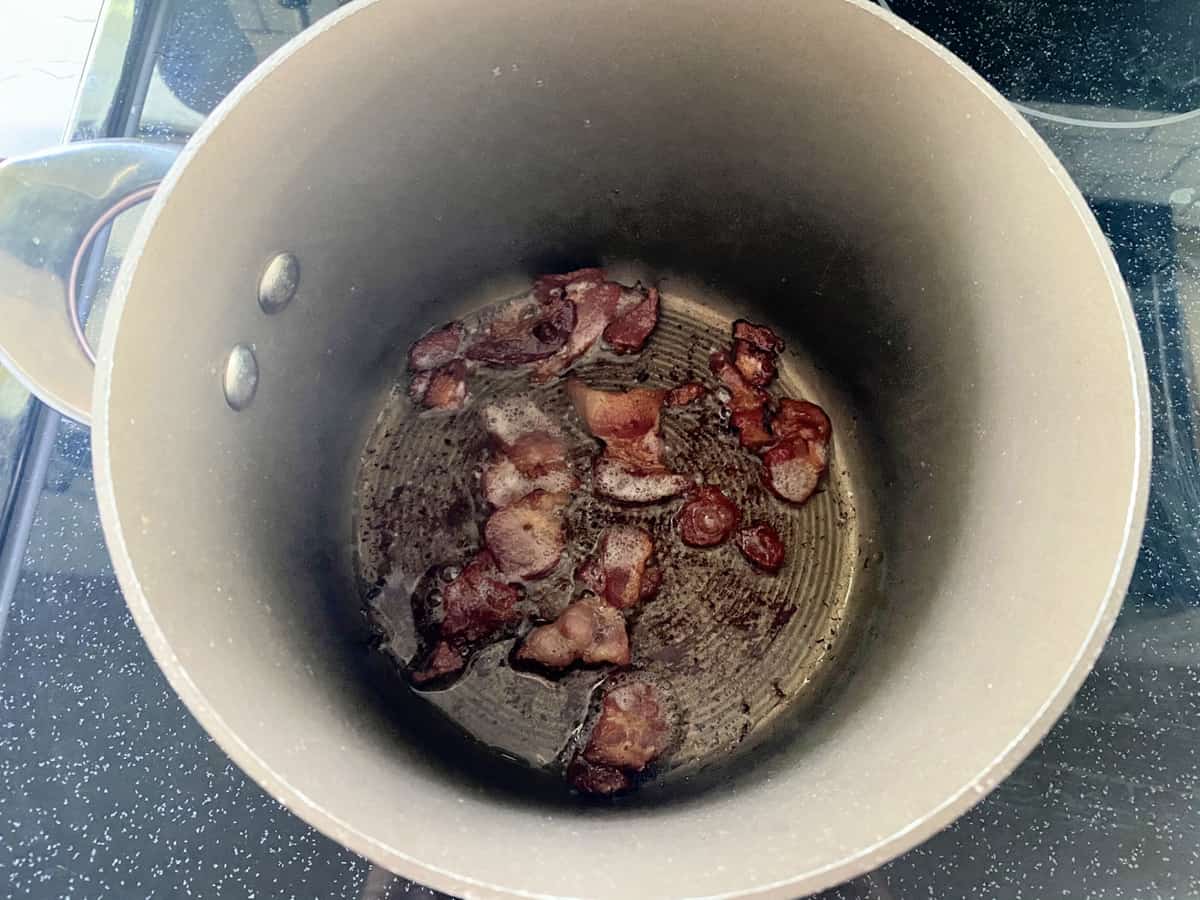 Top view of a brown pot with chopped bacon cooking.