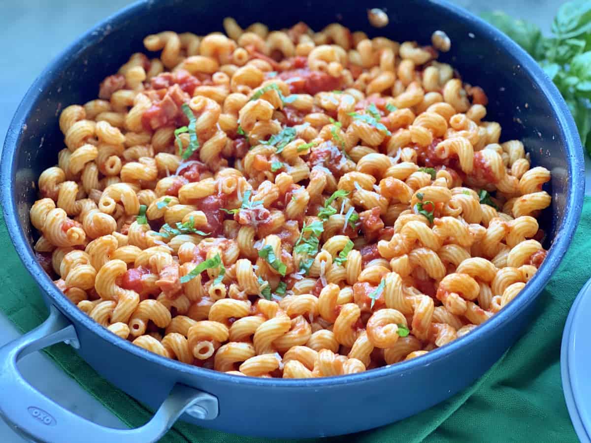 Black OXO skillet filled with corkscrew pasta with basil threads and red sauce.