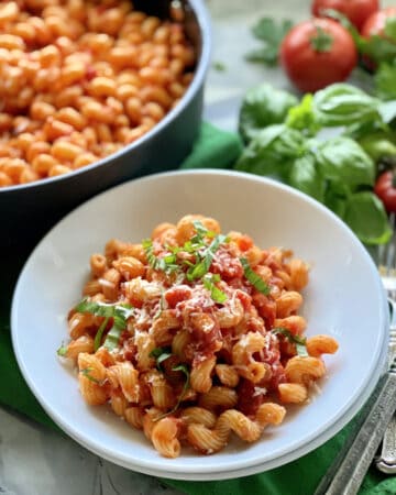 White bowl filled with Cavatappi amatriciana with skillet in the background.